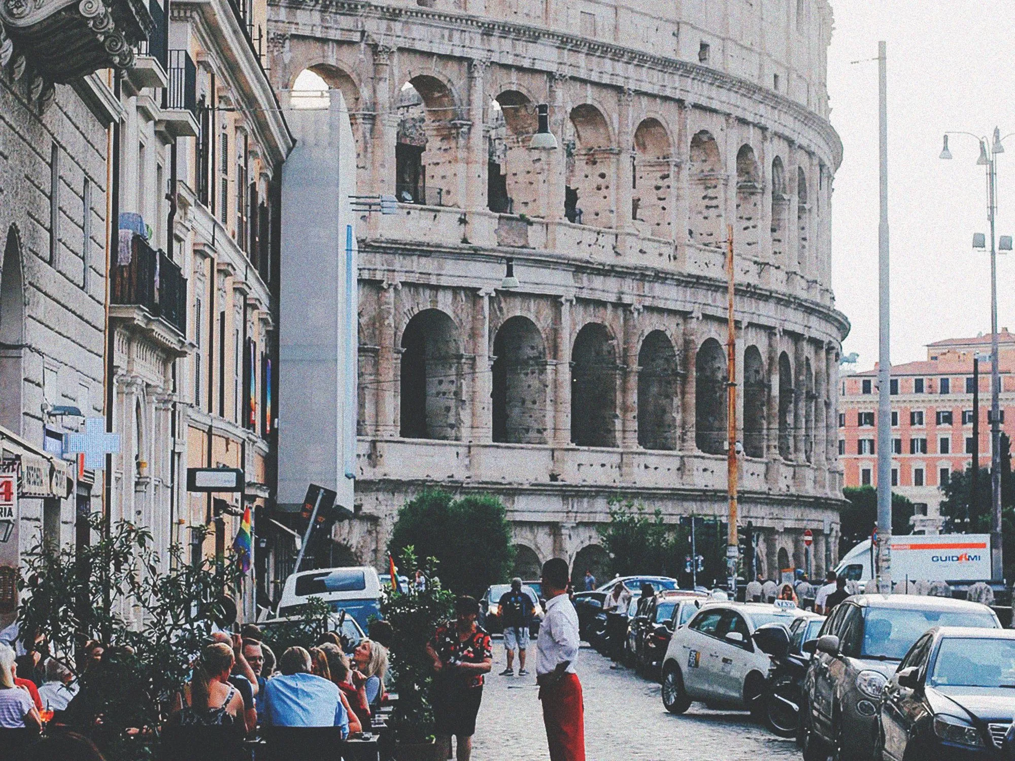 Diners at outdoor tables on a street that ends at the Colosseum